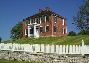 White picket fence in front of colonial house on hill